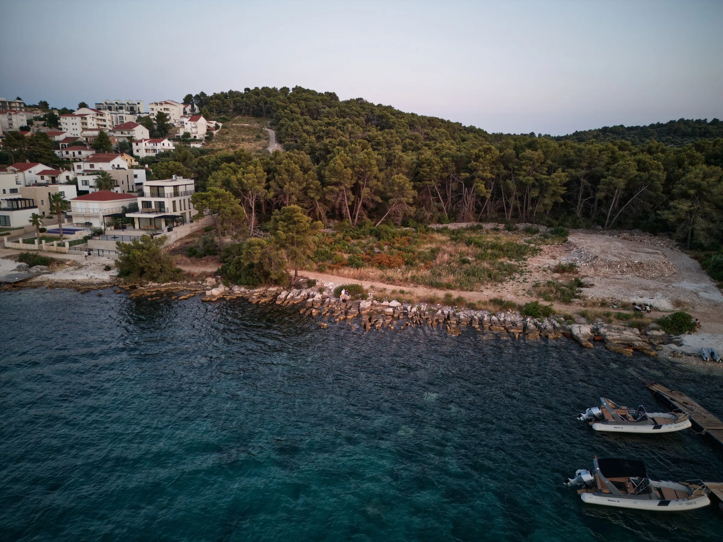 A rocky coastline with houses and pine trees, from above